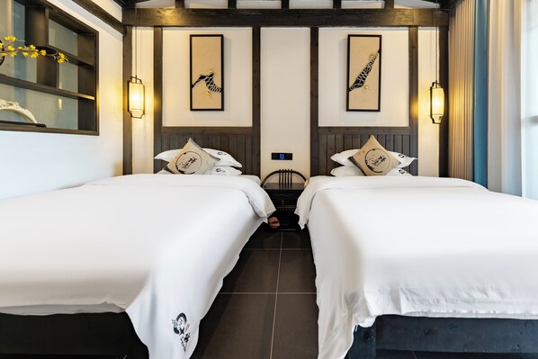 A hotel room with two beds, a large window, wall-mounted artwork, and a modern light fixture.
