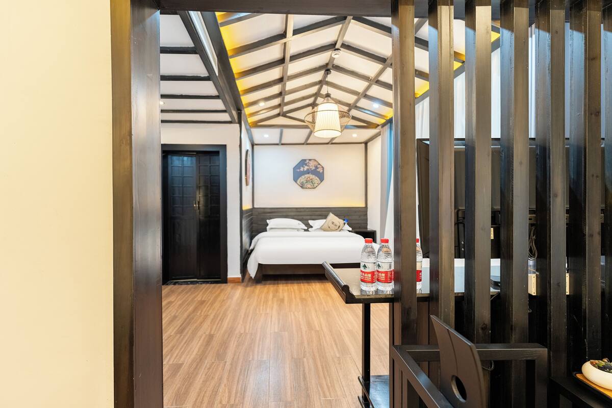 A hotel room with a bed, a nightstand, a wall clock, and a ceiling with wooden beams.