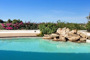 A clear swimming pool with rocks and flowers around it. - Holiday Residence Il Giardino Degli Oleandri in Porto Cervo (Arzachena)