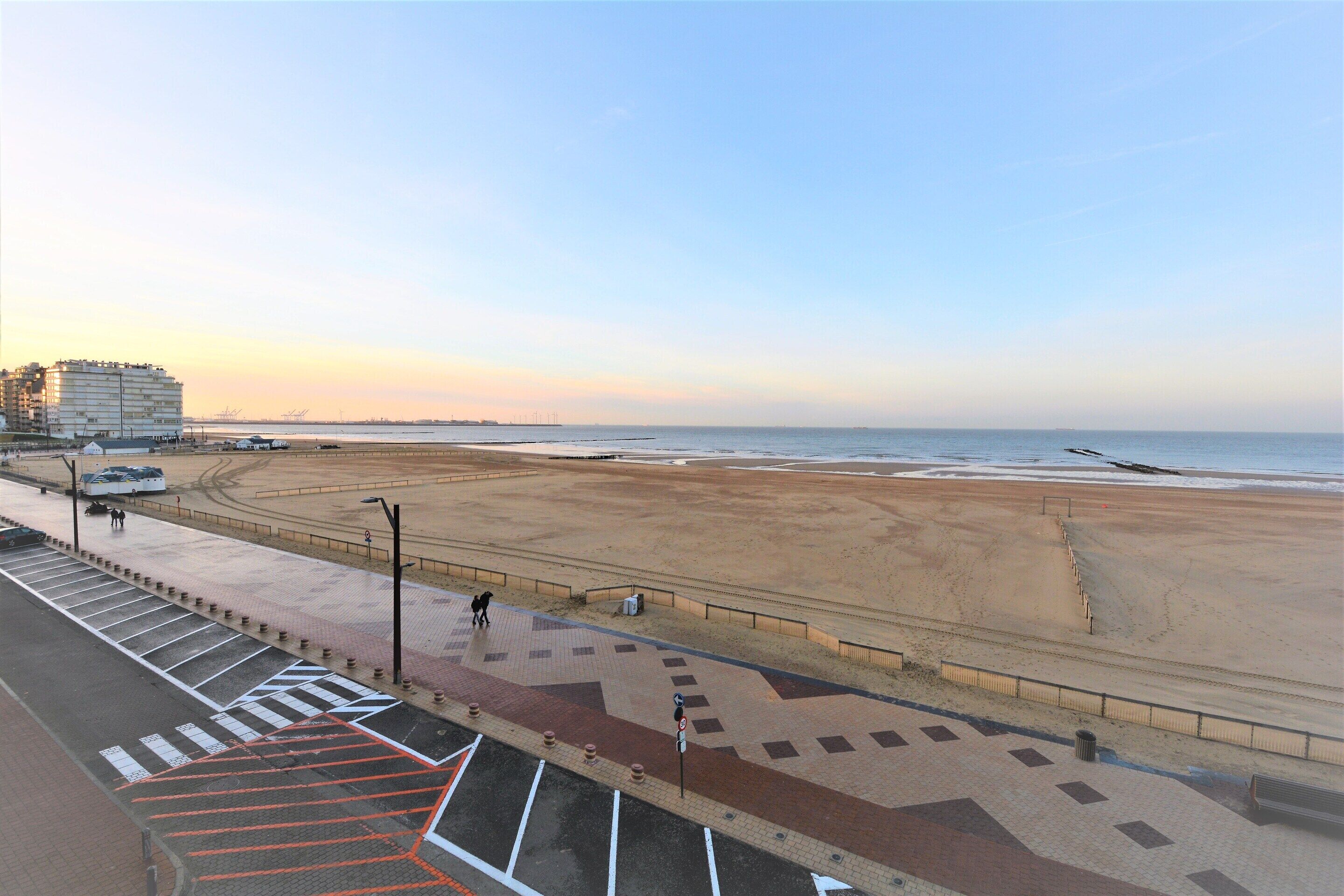 A beach view with a promenade, a building in the background, and a clear sky.