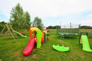 A playground with a swing set, a slide, a trampoline, and a climbing structure. - Holiday Homes With Pool and Jacuzzi (Postomino)