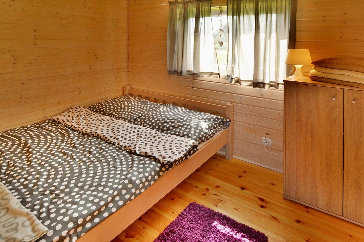 A wooden room with a bed, a window with curtains, a lamp, and a cabinet.