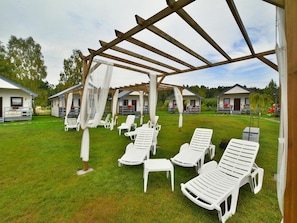 En overdækket udendørs siddeplads med hvide liggestole og en pergola.