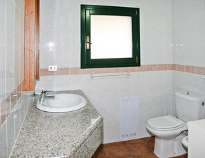 Et badeværelse med vask i granit, et hvidt toilet og et vindue med grøn ramme.