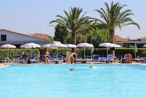A swimming pool with lounge chairs and umbrellas, surrounded by palm trees and buildings. - Villa in Cecina Mare Near Sandy Beach (Cecina)