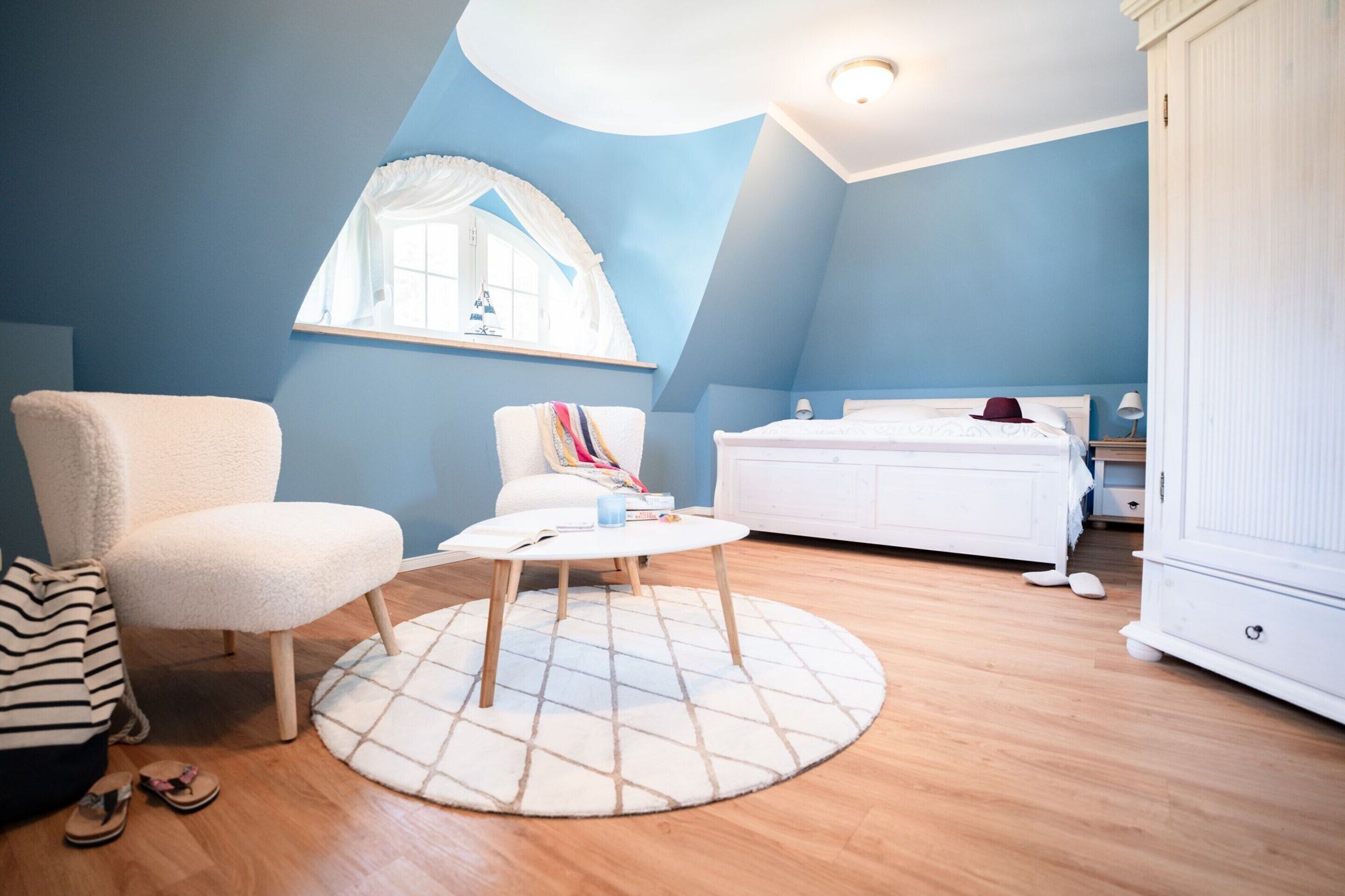 A bedroom with a bed, a chair, a table, and a window.