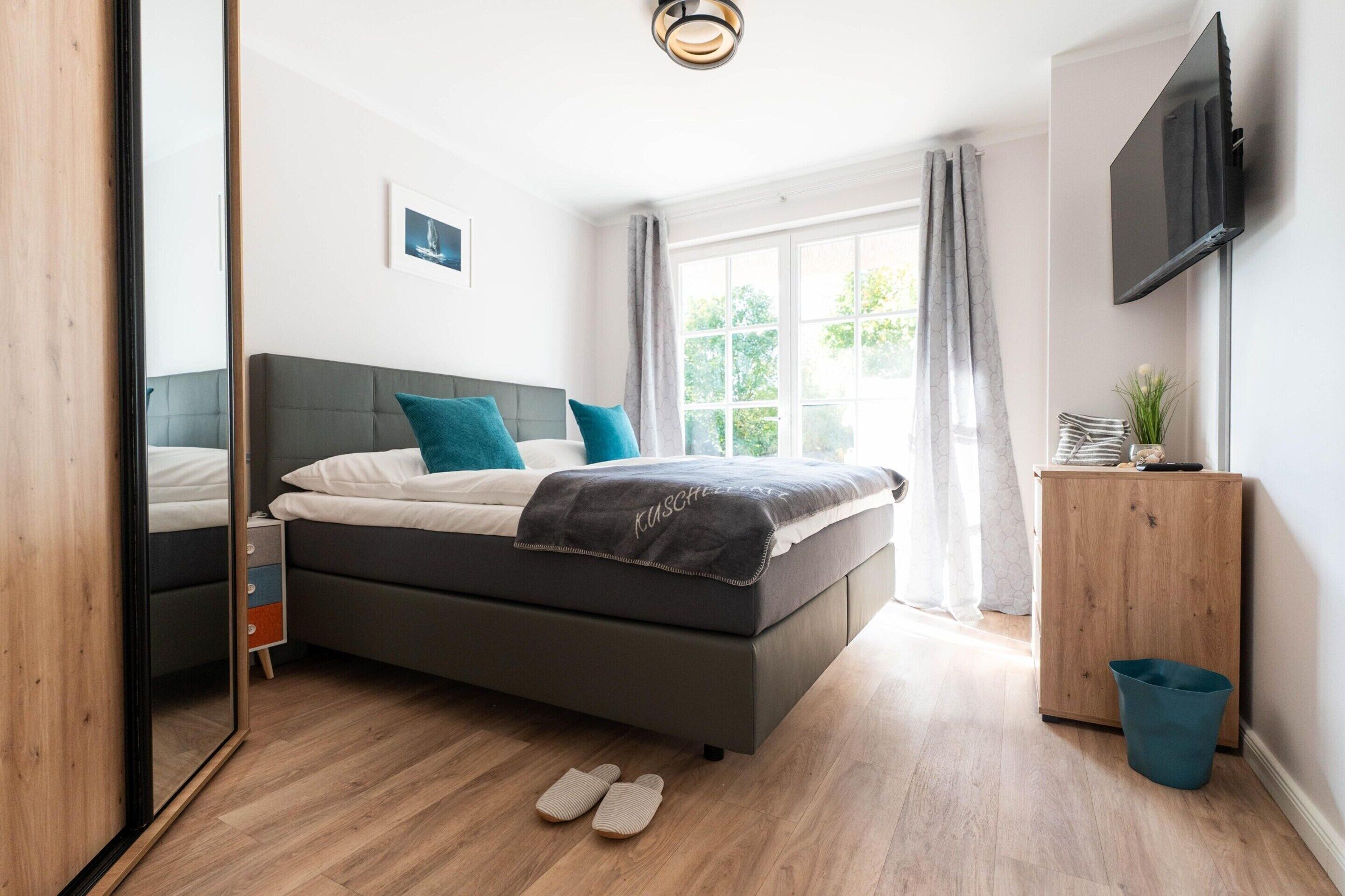 A bedroom with a bed, a wooden cabinet, a television, and a window with curtains.