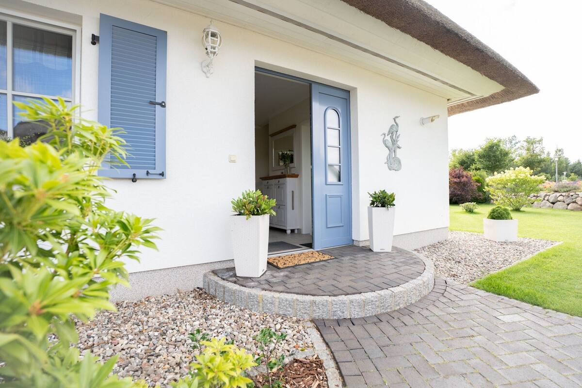 A house with a blue door, a white exterior, and a garden with potted plants.
