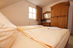 A bedroom with two beds, a wooden wardrobe, a radiator, a window with curtains, and a television on a wooden stand. - Ferienhaus in Wernigerode mit Gemeinschaftspool (Wernigerode)