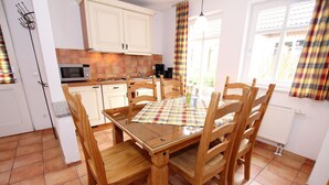 A kitchen with a dining table and chairs, a microwave, and a window with curtains. - Ferienhaus in Wernigerode mit Gemeinschaftspool (Wernigerode)