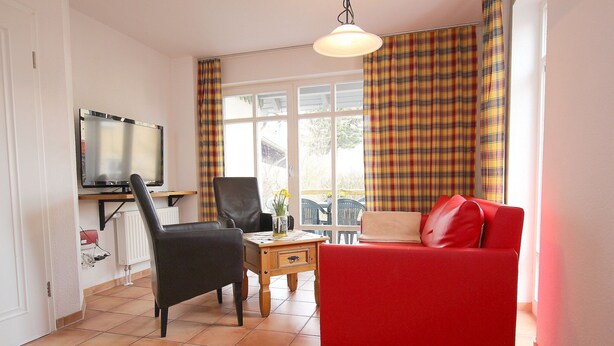 A living room with a red sofa, a black chair, a television, and a window with plaid curtains. - Ferienhaus in Wernigerode mit Gemeinschaftspool (Wernigerode)