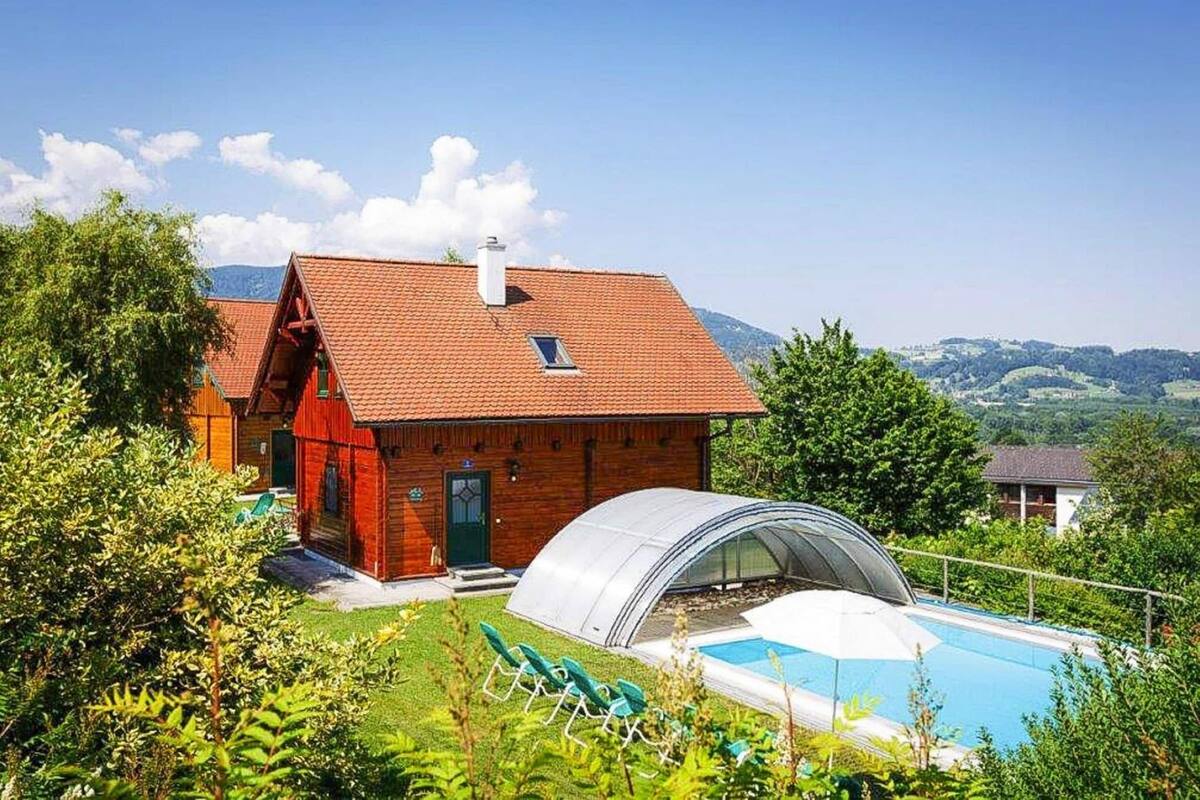 A wooden house with a red roof, a swimming pool, and a greenhouse.