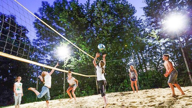 A group of people playing volleyball on a sandy court with a net, surrounded by trees and under bright lights. - Chalet Near Kalkalpen National Park (Schlierbach)