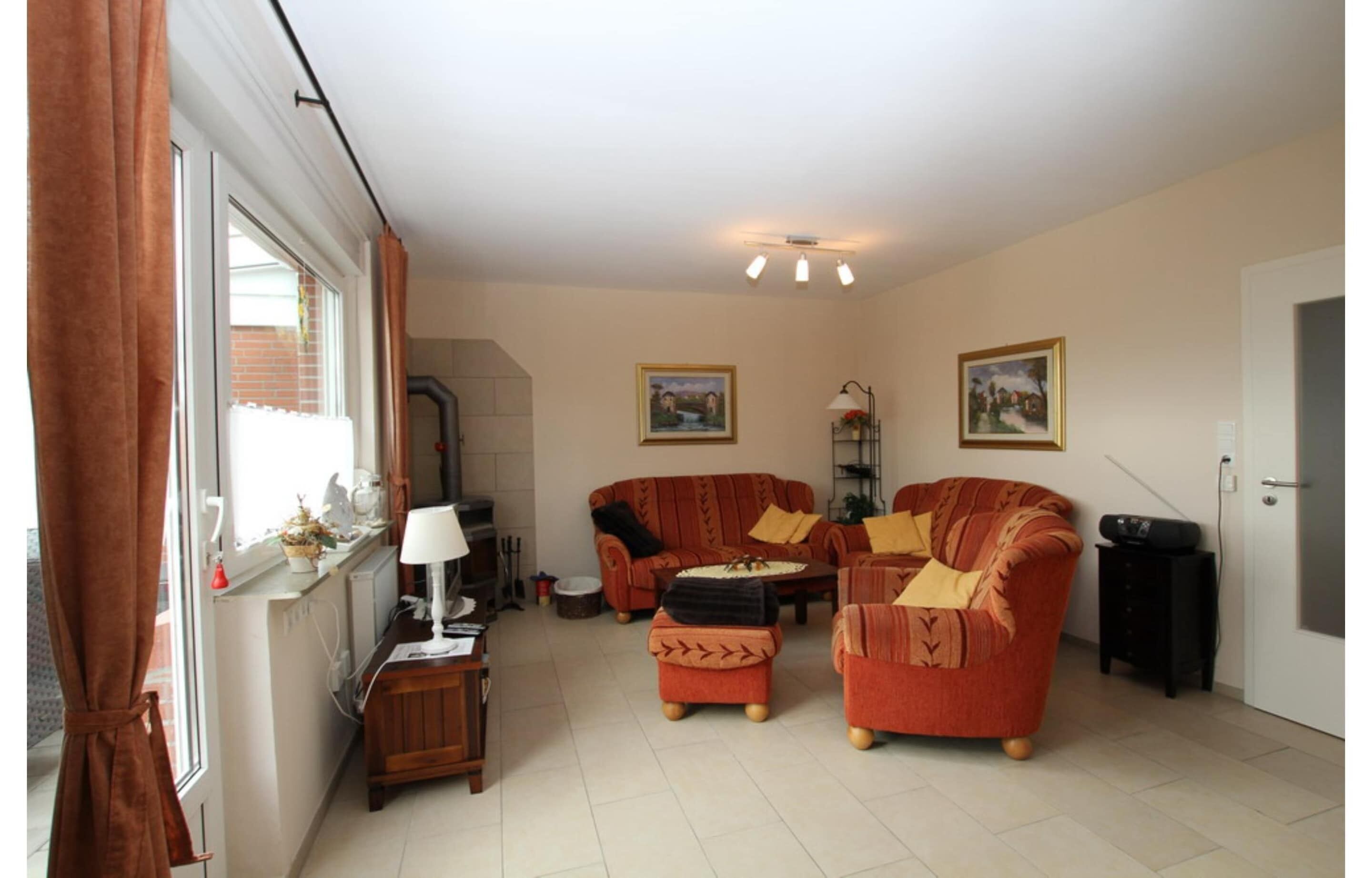 Sala de estar con dos sofás, una mesa de centro, una lámpara y un radiador. Hay dos cuadros en la pared y una ventana con cortinas.