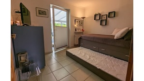 A bedroom with a bed, a desk, a chair, a radiator, and a door leading to an outdoor area. - Strandnaher Bungalow in Dornumersiel (Dornum)