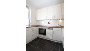 A kitchen with white cabinets, a black oven, and a tiled floor. - Strandnaher Bungalow in Dornumersiel (Dornum)
