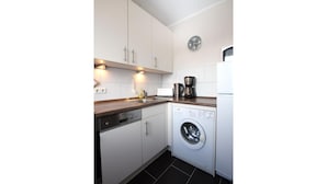 A compact kitchen with white cabinets, a dishwasher, a washing machine, and a coffee maker. - Strandnaher Bungalow in Dornumersiel (Dornum)