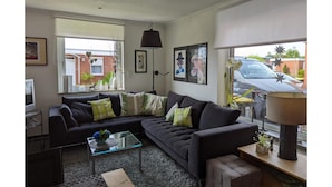A living room with a sectional sofa, a glass coffee table, and a lamp. - Strandnaher Bungalow in Dornumersiel (Dornum)
