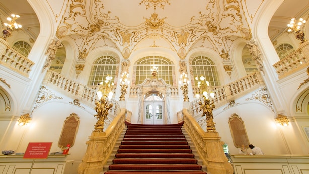 Una gran escalera con detalles ornamentales dorados y una alfombra roja, que conduce a un amplio arco.