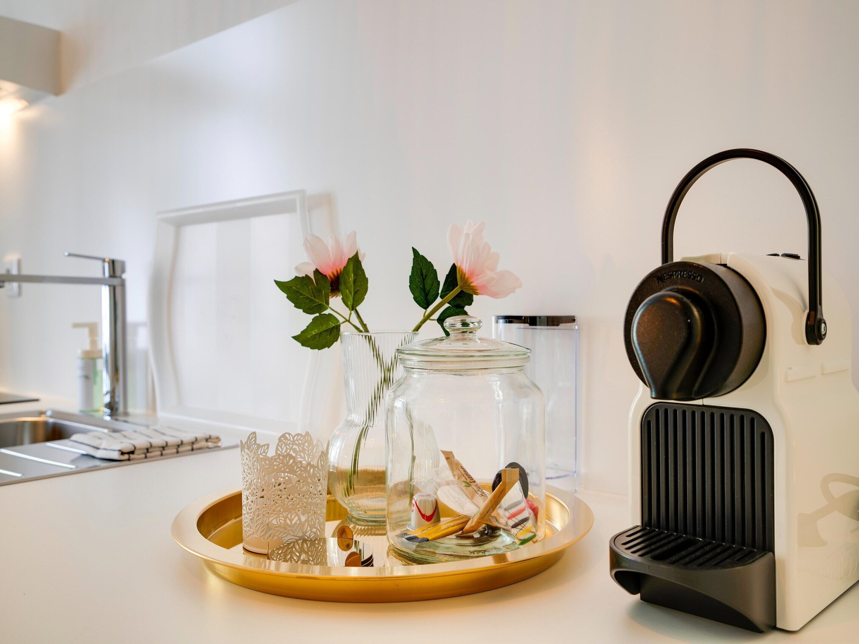 En köksbänk med en kaffemaskin, en glasburk med en blomma och ett bricka med en dekorativ prydnad.