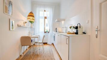 Una cucina moderna con mobili bianchi, una zona pranzo con tavolo e sedie, un lampadario e vista all'esterno da una finestra.
