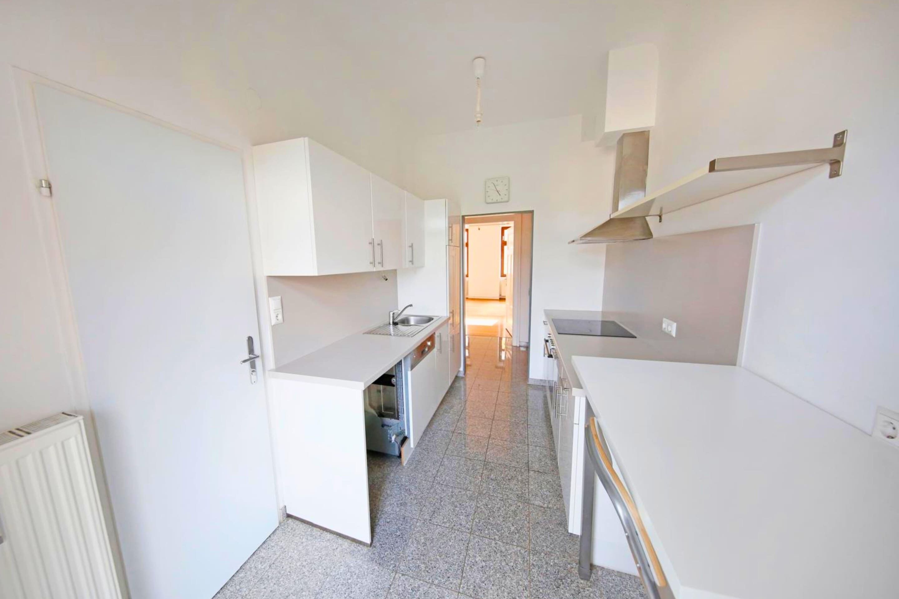 A narrow kitchen with white cabinets, a sink, and a stove.