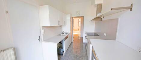 A narrow kitchen with white cabinets, a sink, and a stove.
