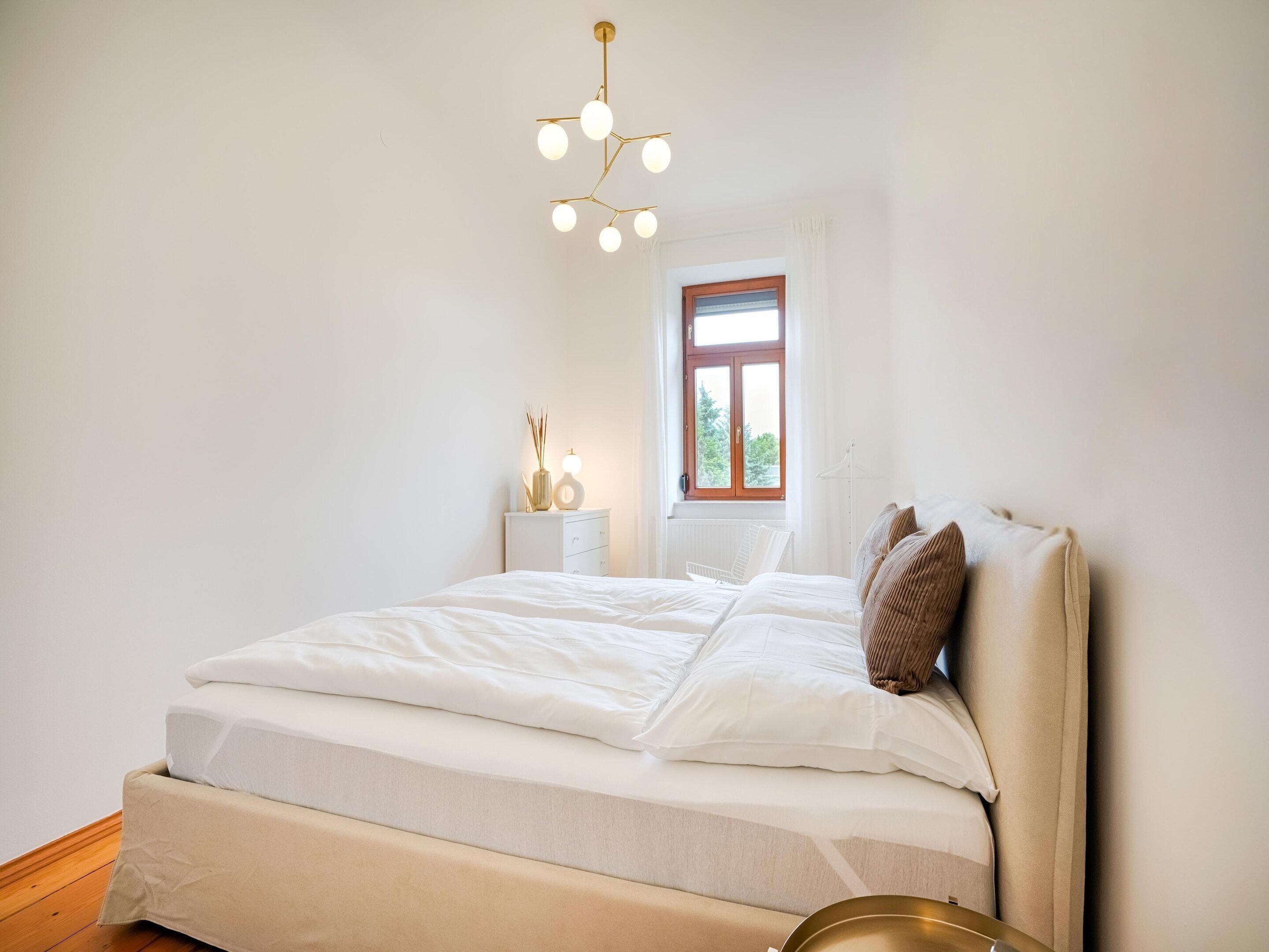 A bedroom with a bed, bedside table, lamp, window, and a hanging light fixture.