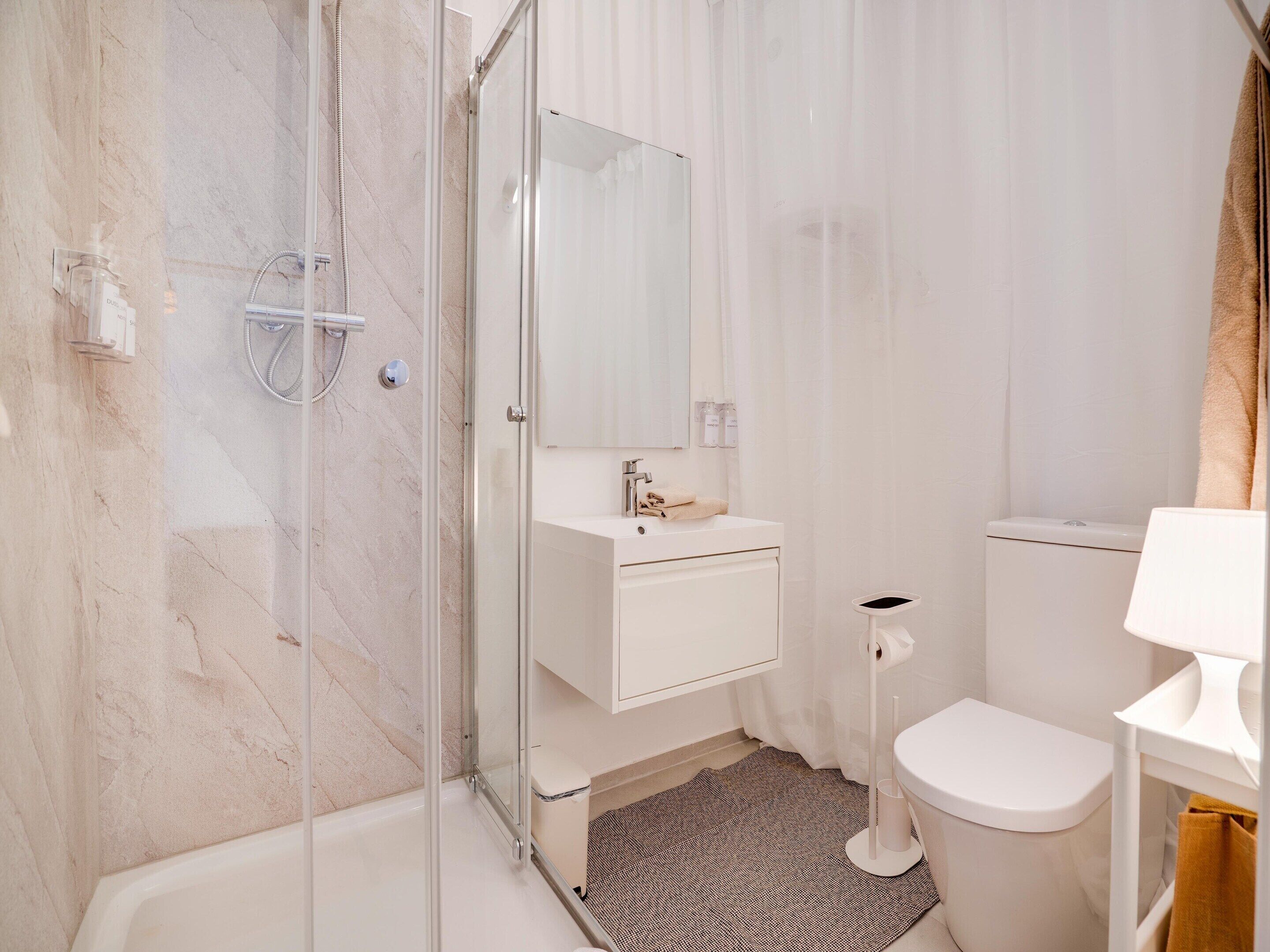A modern bathroom with a glass shower enclosure, a white sink, and a toilet.