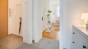 Un pasillo con una puerta, un teléfono, un paraguas, una silla y una mesa con una lámpara.