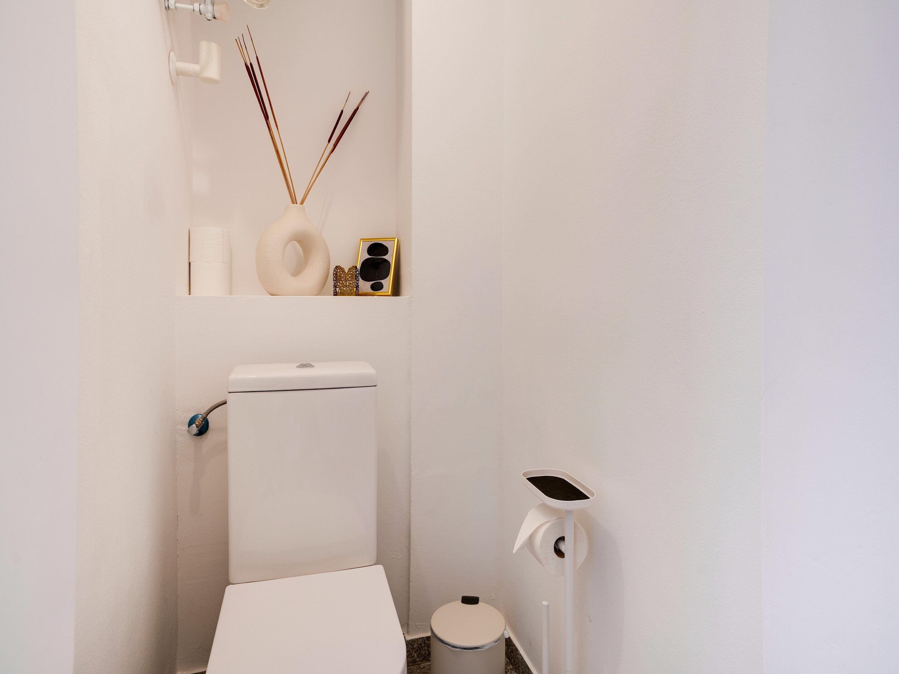 A small, white bathroom with a toilet, bidet, and a wall-mounted toilet paper holder.