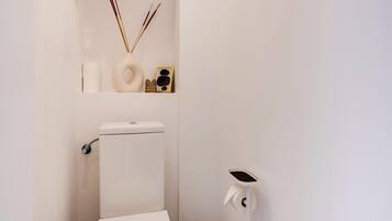 A small, white bathroom with a toilet, bidet, and a wall-mounted toilet paper holder.
