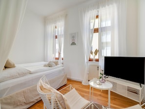 Quarto com duas camas, televisão e uma pequena mesa com um vaso.