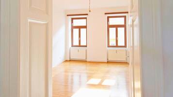 Una habitación vacía con pisos de madera, dos ventanas con marcos de madera y un radiador debajo de cada ventana.