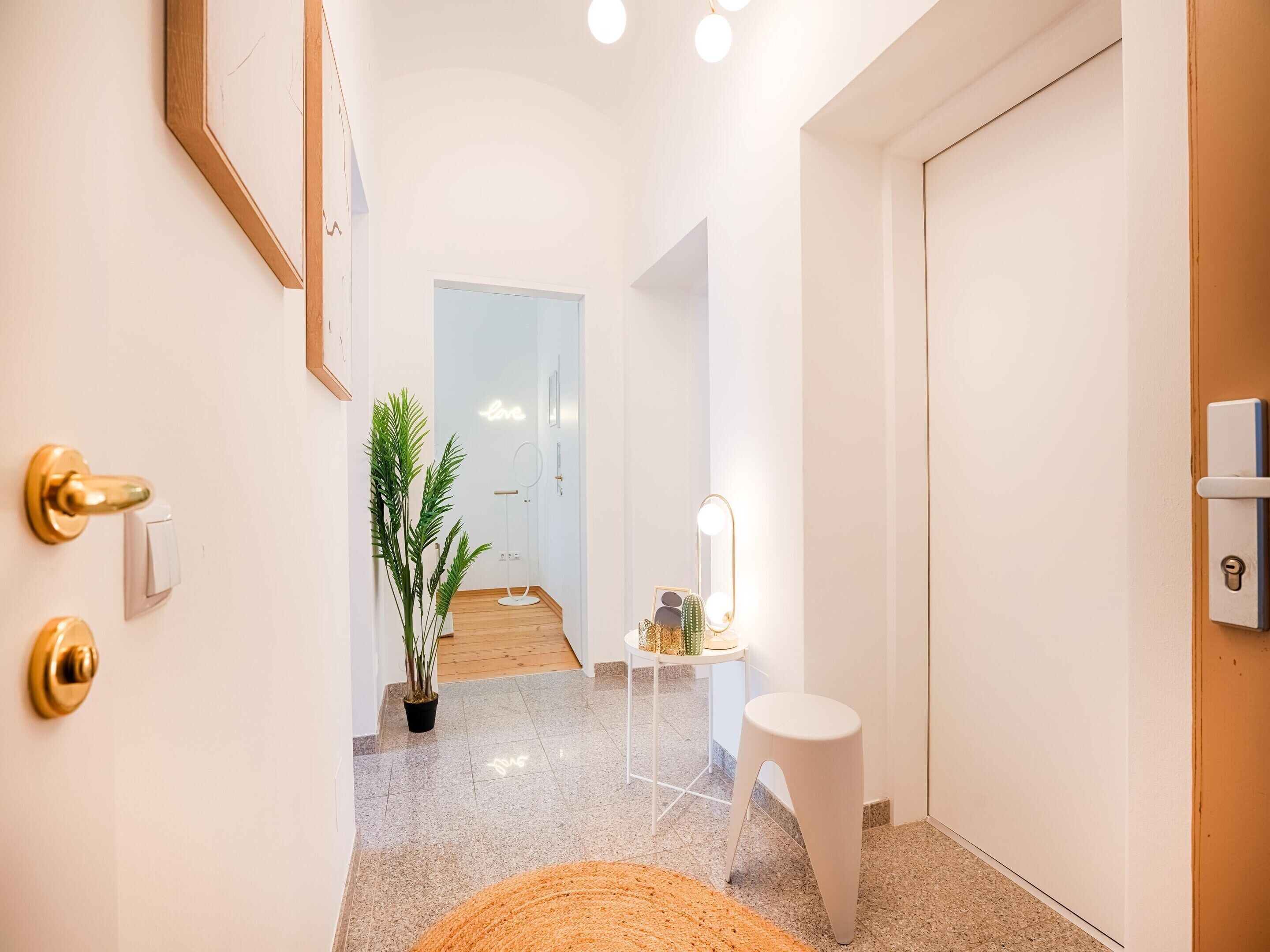 A hallway with a potted plant, a small table with a mirror, and a white door.