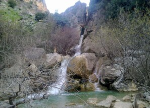 Een natuurlijke waterval omringd door rotsachtig terrein en schaarse begroeiing.