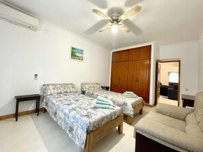 Een slaapkamer met twee bedden, een plafondventilator, een houten garderobe en een stoel.