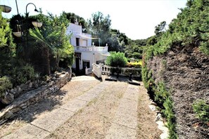 A white building with a balcony, surrounded by greenery and a stone wall. - Apartment in Playa de Pals Near Sandy Beach (Pals)