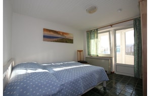 A bedroom with two beds, a window with curtains, a radiator, and a painting on the wall. - Bungalow in Strandnaehe, Dornumersiel (Dornum)