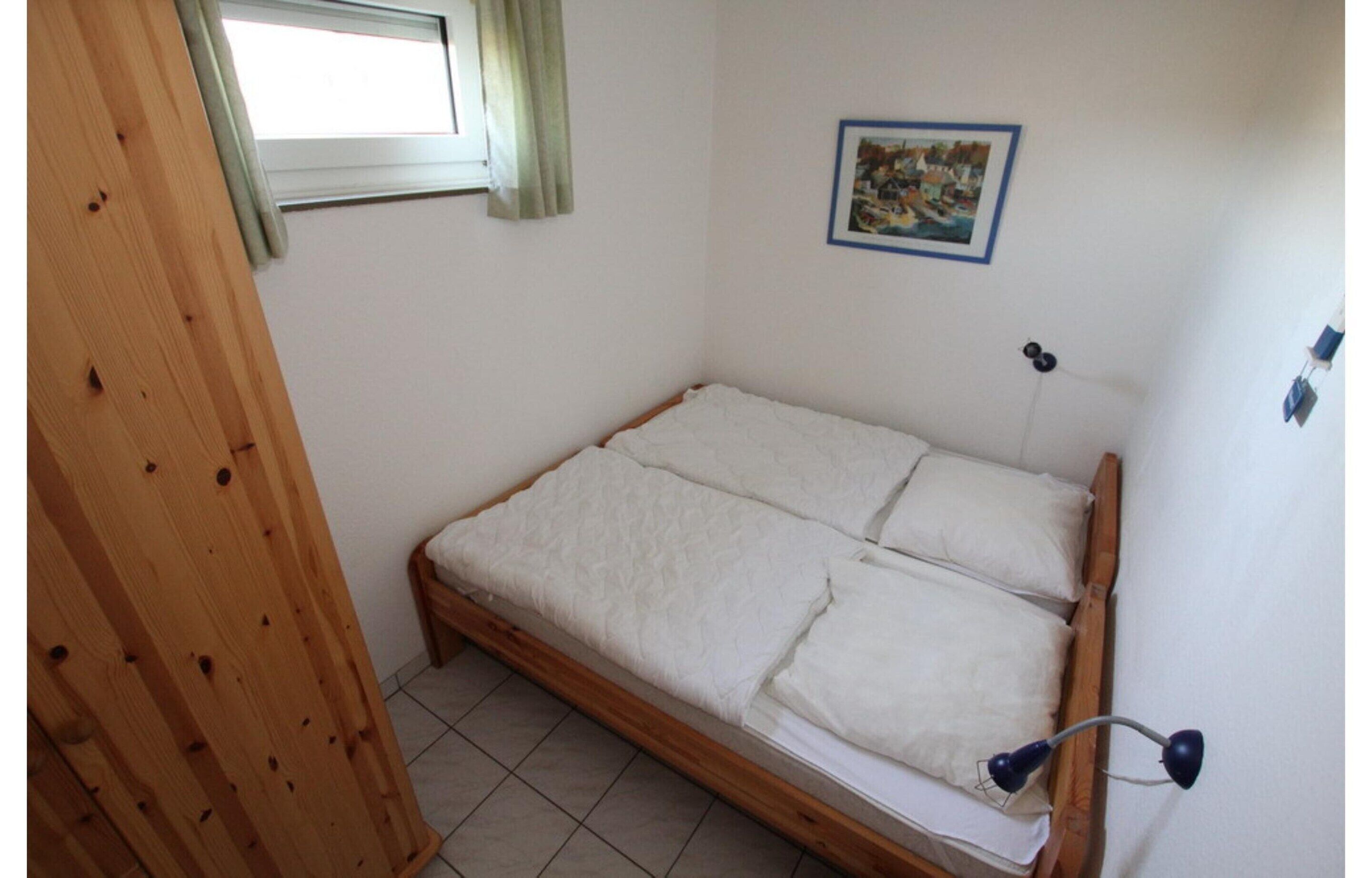 Een enkel bed met houten frame, een raam met gordijn, een aan de muur hangend schilderij en een bedlampje.