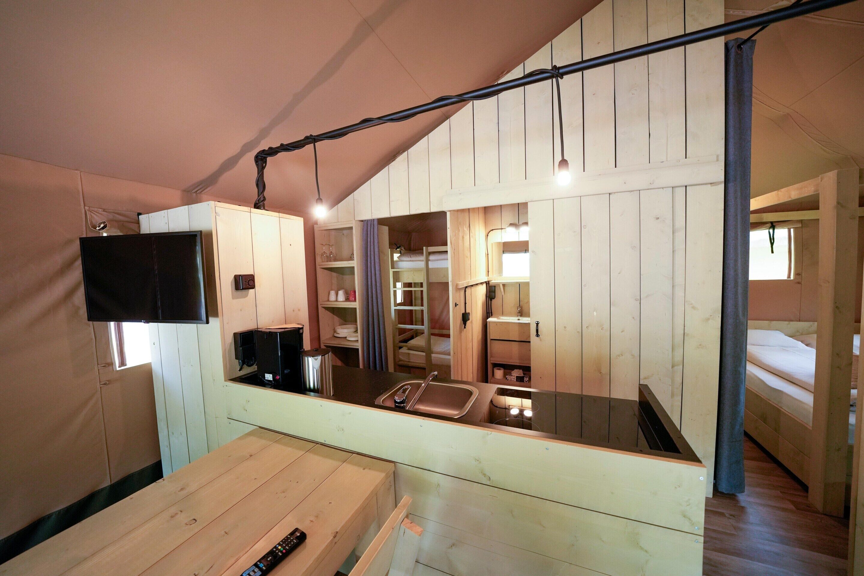 A compact, wooden interior with a kitchenette, a TV mounted on the wall, and a bed with a window.