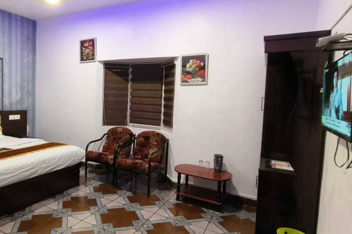 Une chambre d’hôtel avec un lit, une chaise, une petite table, un téléviseur et une fenêtre avec des stores.