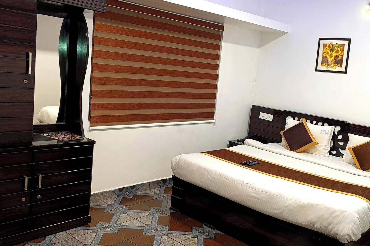 Une chambre à coucher avec un lit, une commode, une fenêtre avec des stores et un tableau encadré au mur.