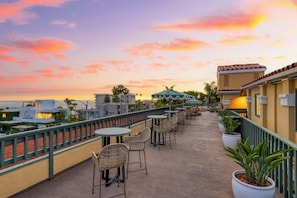 Una terrazza sul tetto con posti a sedere all'aperto, vista sull'oceano e un cielo al tramonto.