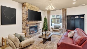 A living room with a stone fireplace, a flat-screen TV, a red leather sofa, and a Christmas tree. - Rooftop Lounge + Hot Tub + Karaoke + Firepit | Katie Hill Collection (Nashville)