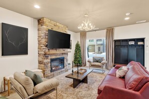 A living room with a stone fireplace, a flat-screen TV, a red leather sofa, and a Christmas tree. - Rooftop Lounge + Hot Tub + Karaoke + Firepit | Katie Hill Collection (Nashville)