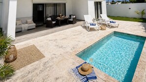 Area piscina moderna all'aperto, con zona relax coperta, lettini e un tavolino.