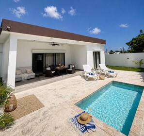 A modern outdoor pool area with a covered seating area, lounge chairs, and a small table. - Modern 2BR Villa with Private Pool, Starlink WiFi,  Security, Near Macao Beach (Higüey)