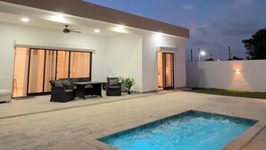 Area piscina moderna all'aperto con zona relax coperta e accesso tramite vetrata scorrevole.