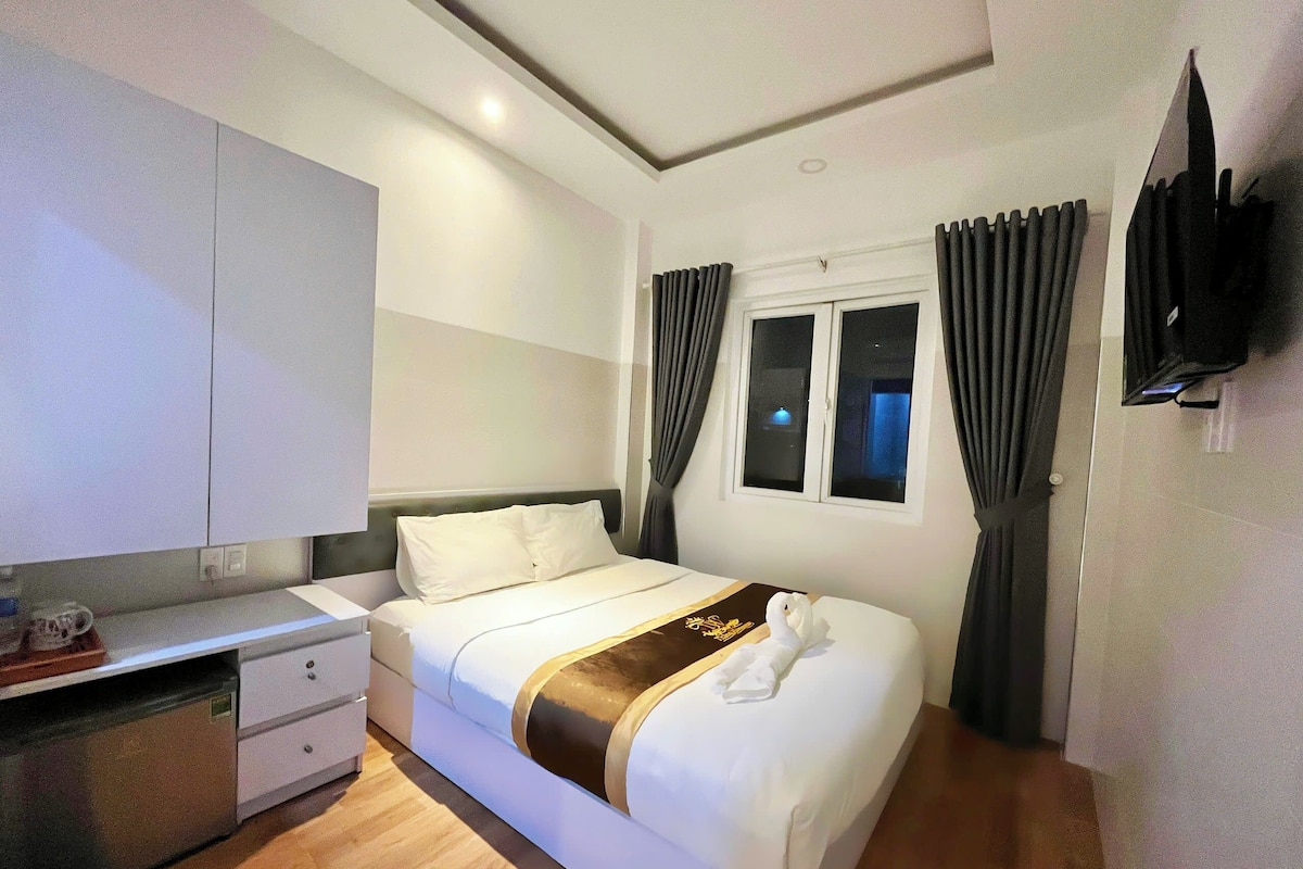 A hotel room with a bed, a desk, a television, and a window with curtains.